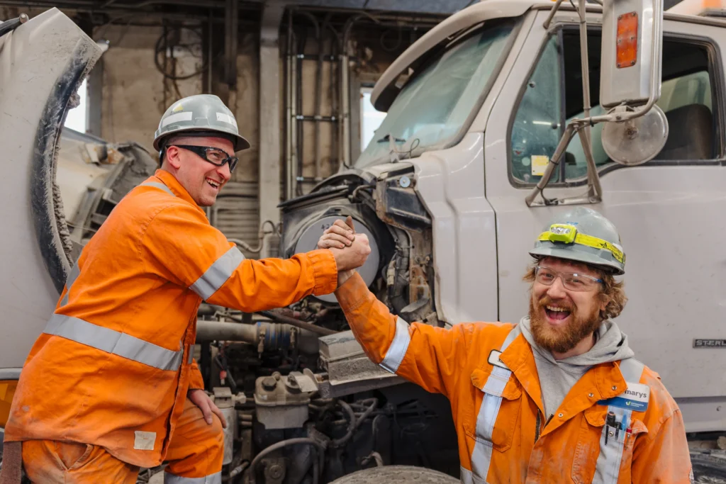 Safety in the Cement Industry - two maintenance workers in orange coveralls high-fiving beside an open truck engine