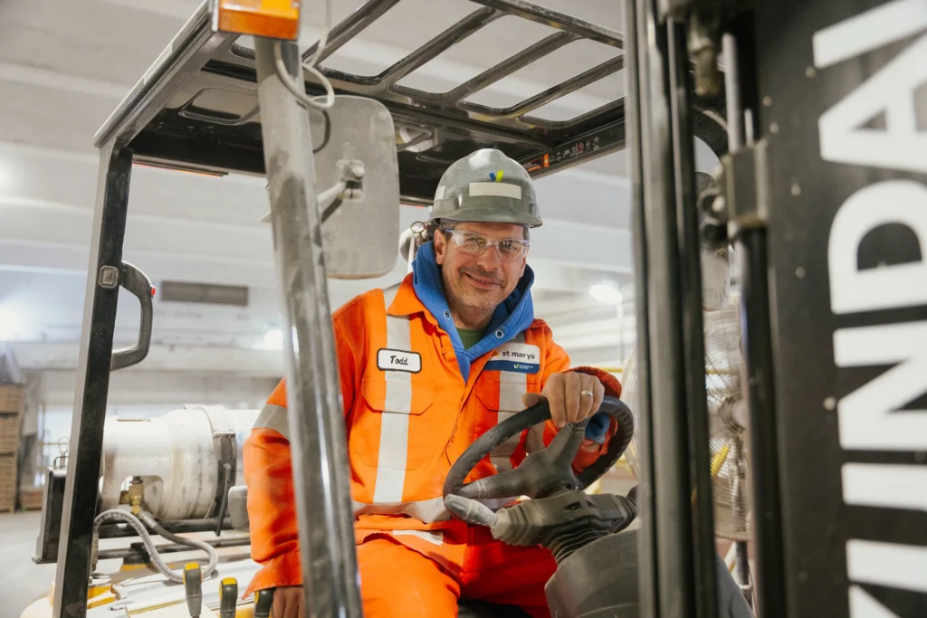 Cement Supplier - smiling forklift operator in orange coveralls and a hard hat in the warehouse