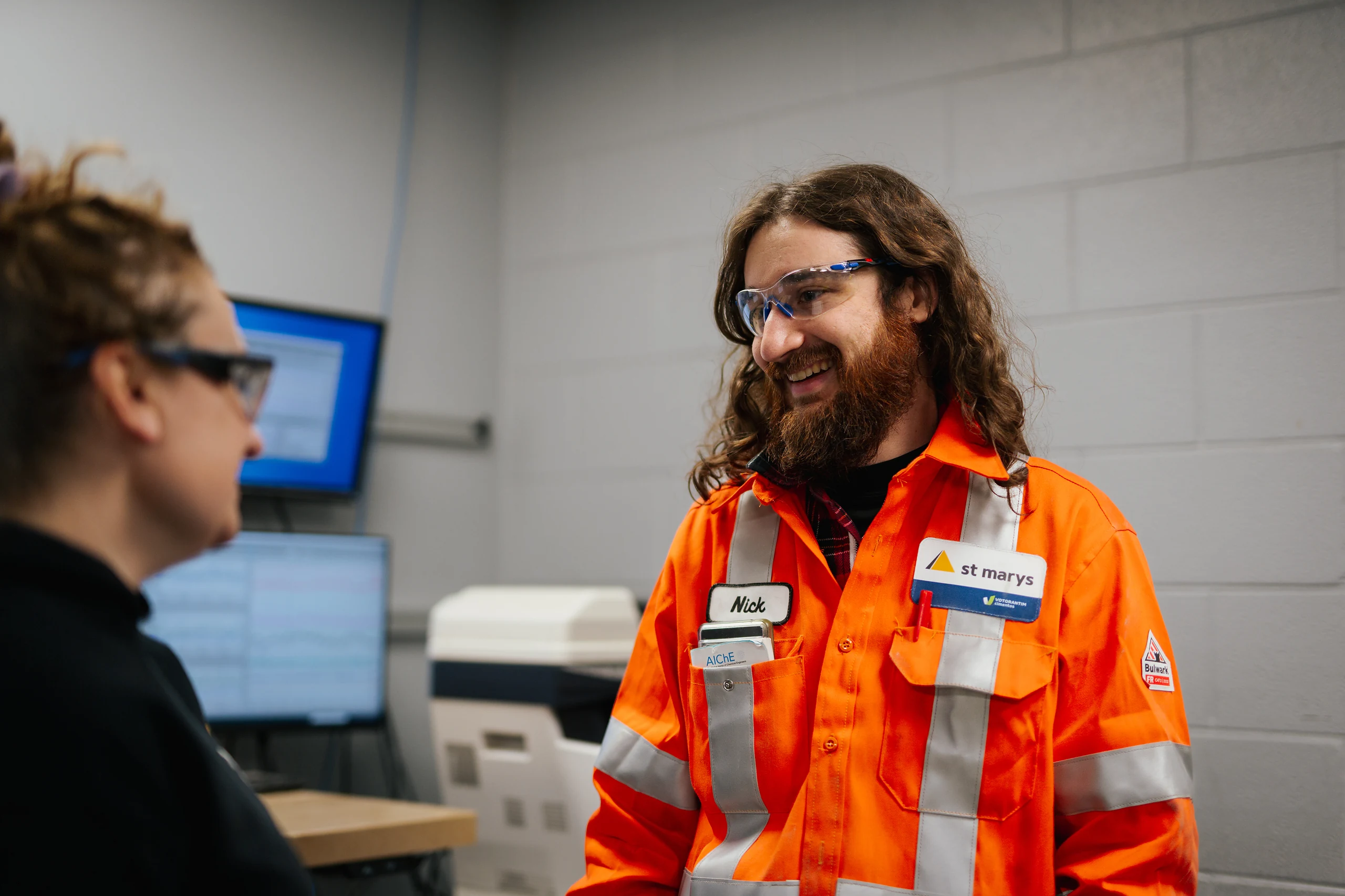 Cement Supplier - St Marys Cement team member in orange coveralls talking with a colleague at a computer workstation