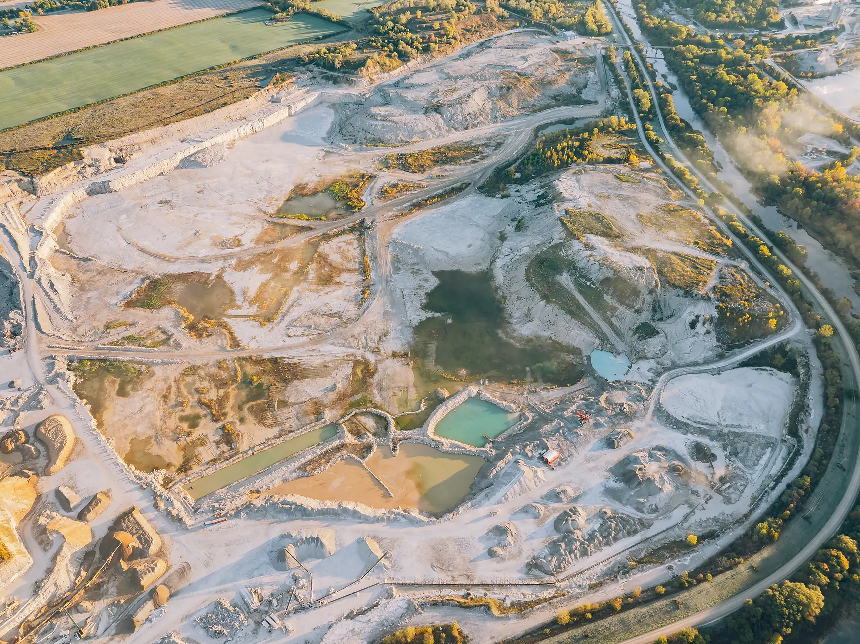 Broad quarry pit seen from height, bleached limestone floor dotted with green and turquoise water pools
