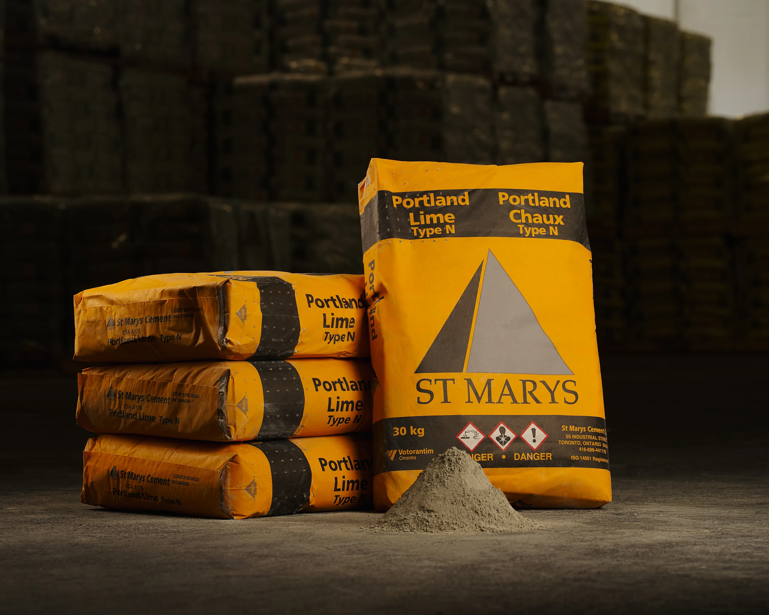 Orange St Marys Portland Lime Type N bags stacked in a warehouse beside a cone of grey powder