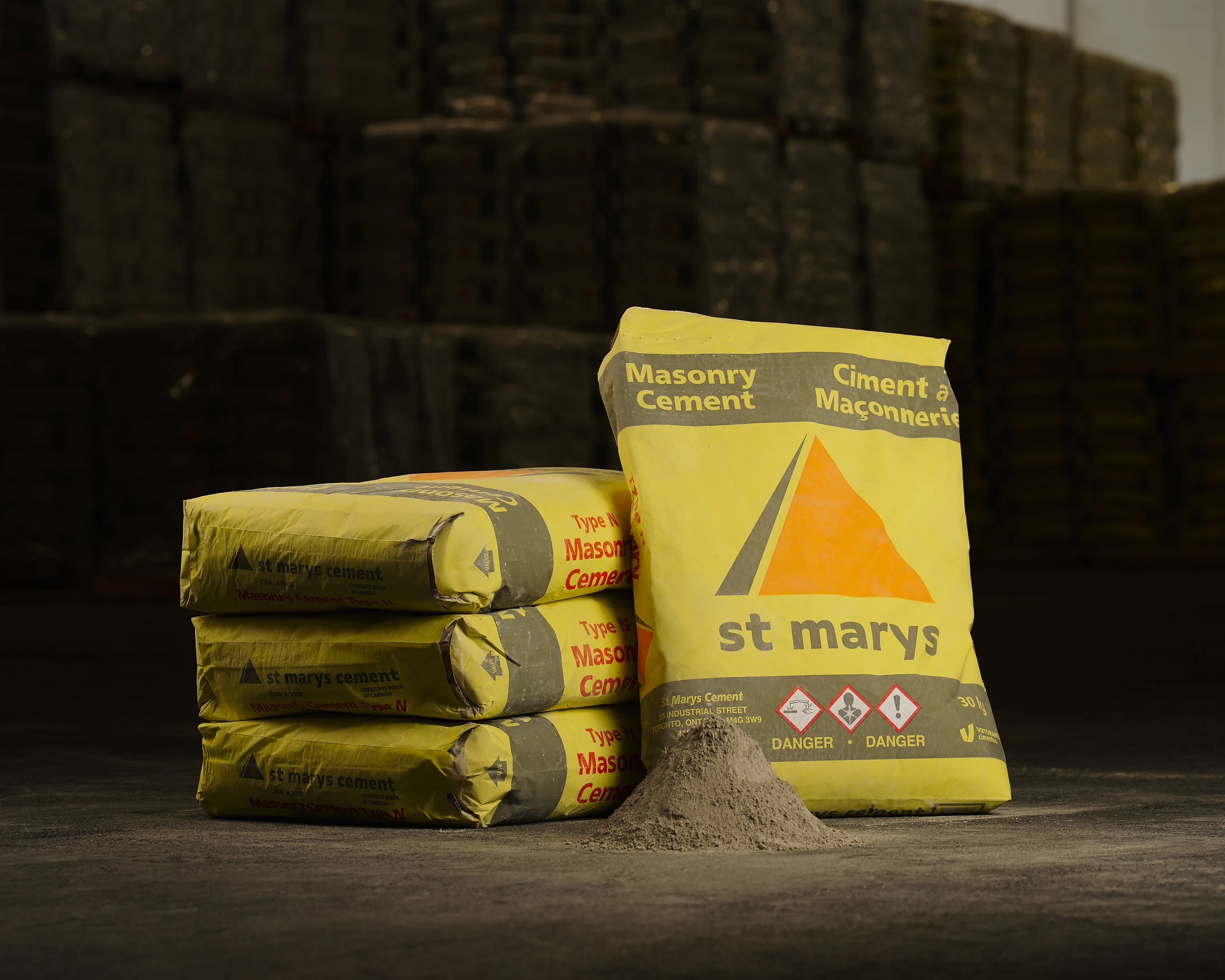 Yellow St Marys Masonry Cement bags stacked and standing in a warehouse beside a cone of powder