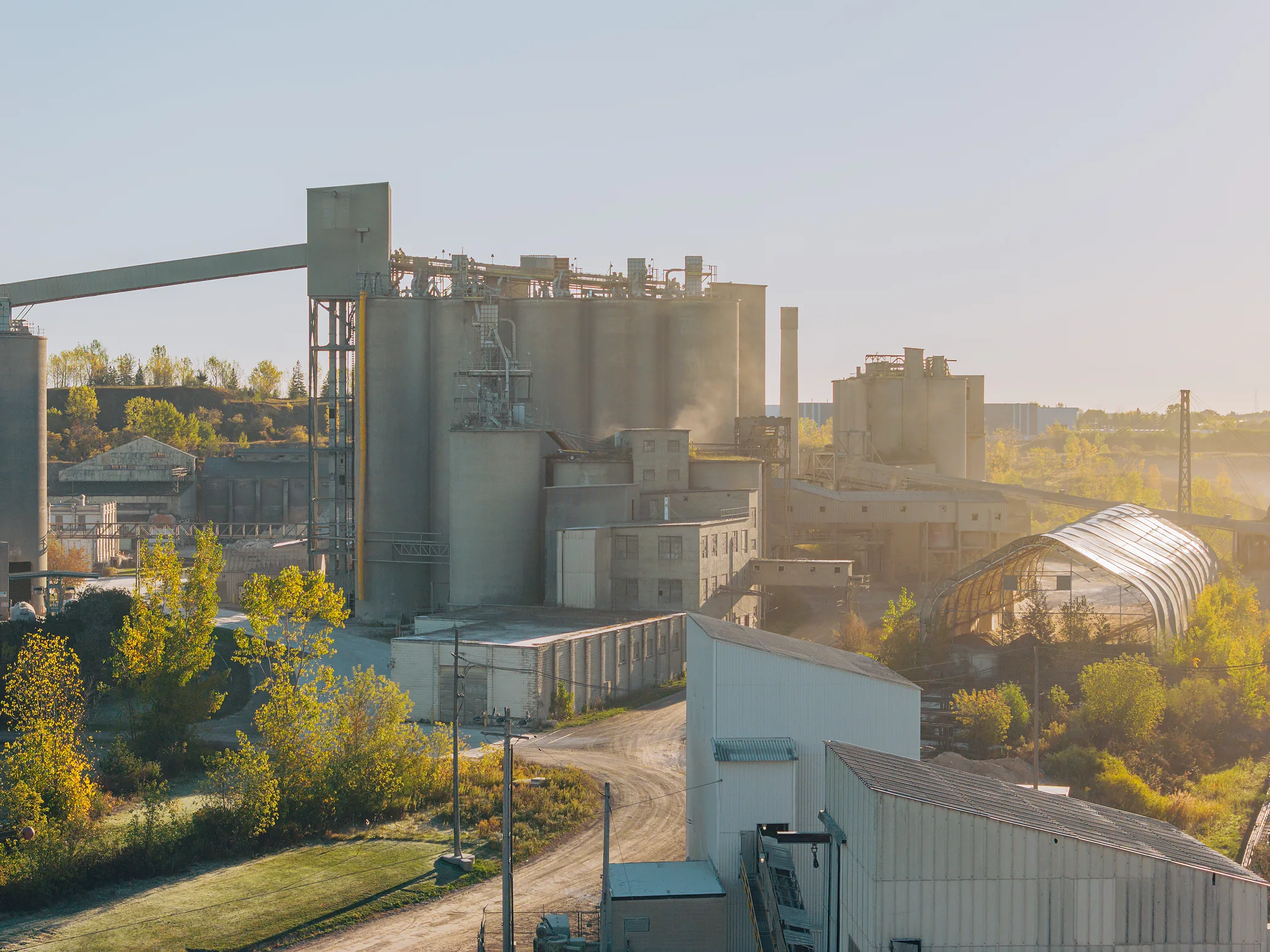 Type S Hi-Bond Mortar Cement - cement plant silos and conveyor gantry behind trees, with a storage dome on the right