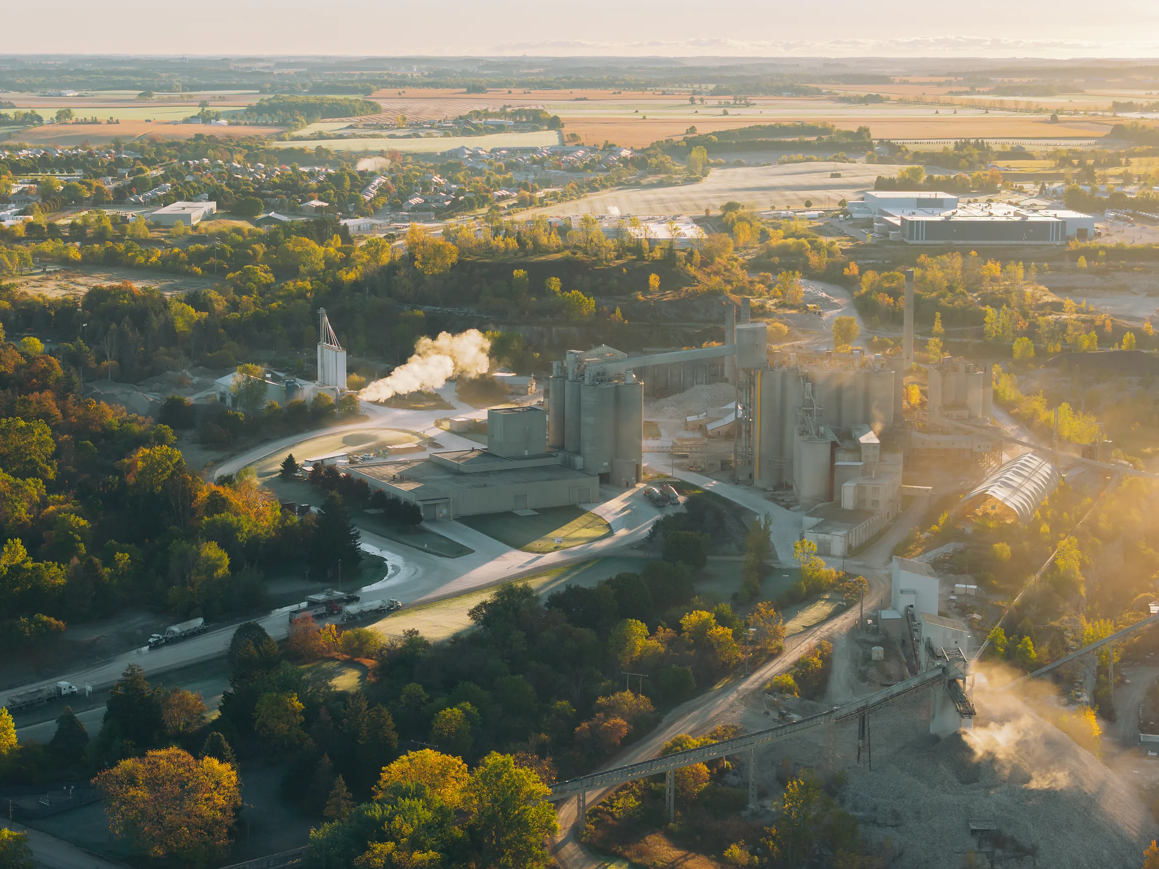 Golden light across the cement works, conveyor bridge at lower right and farmland stretching to the horizon