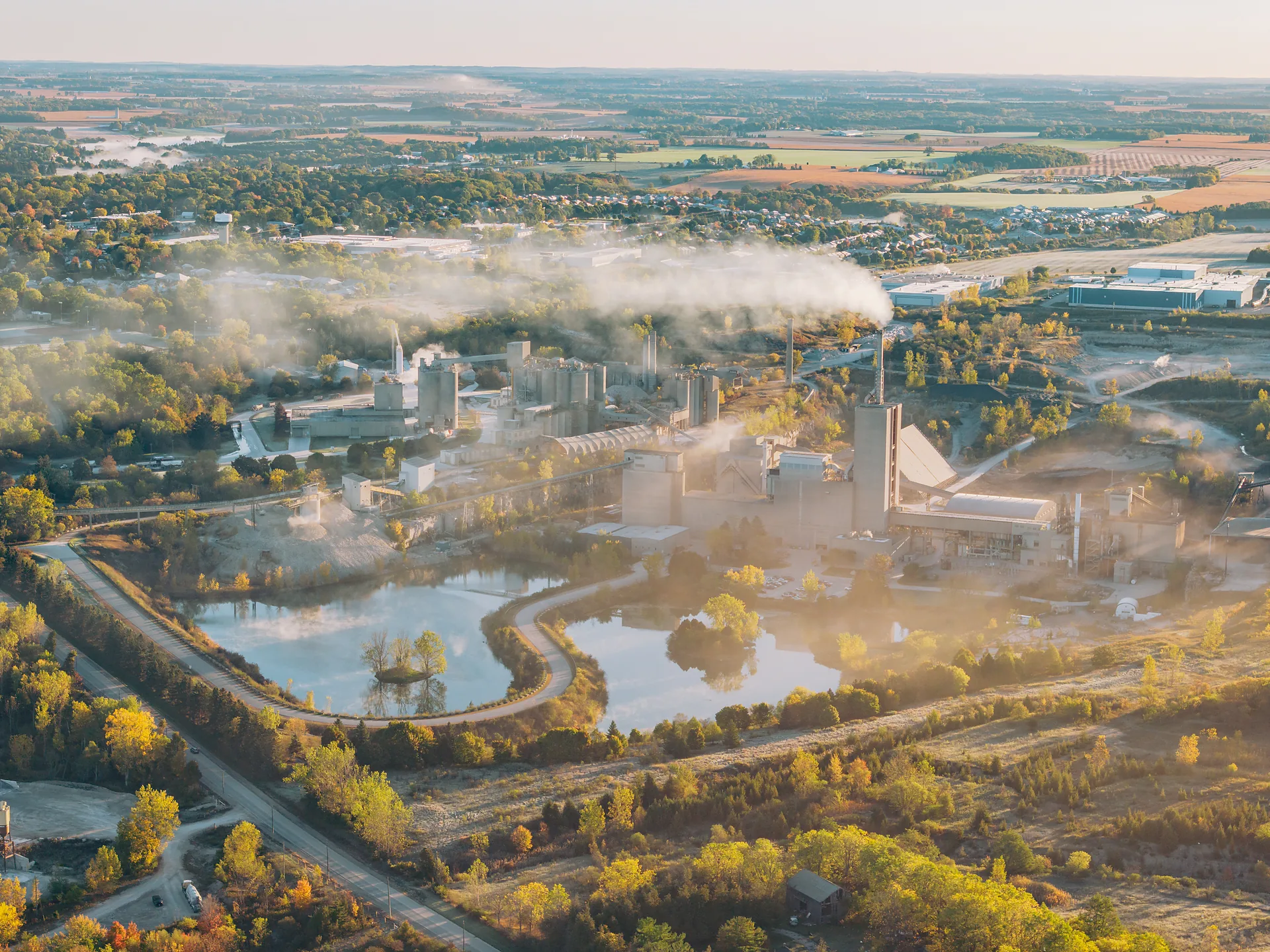 Type I/II Cement - aerial view of the cement plant beside two quarry ponds, with the kiln plume and town beyond