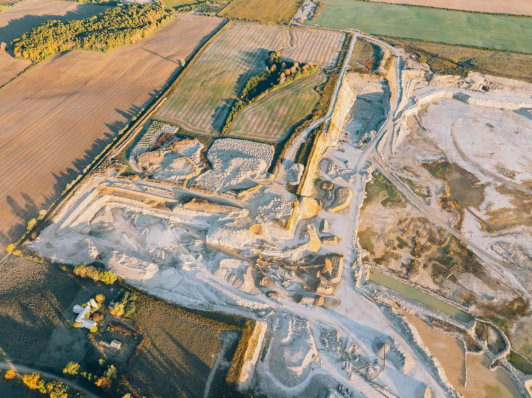 Type 1L Cement - overhead aerial view of the limestone quarry floor, stockpiles and haul roads beside farm fields