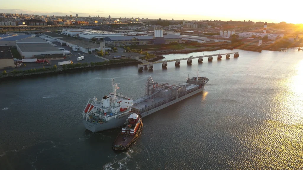 Verdera - cement carrier ship with a tug alongside at a riverside terminal at dusk