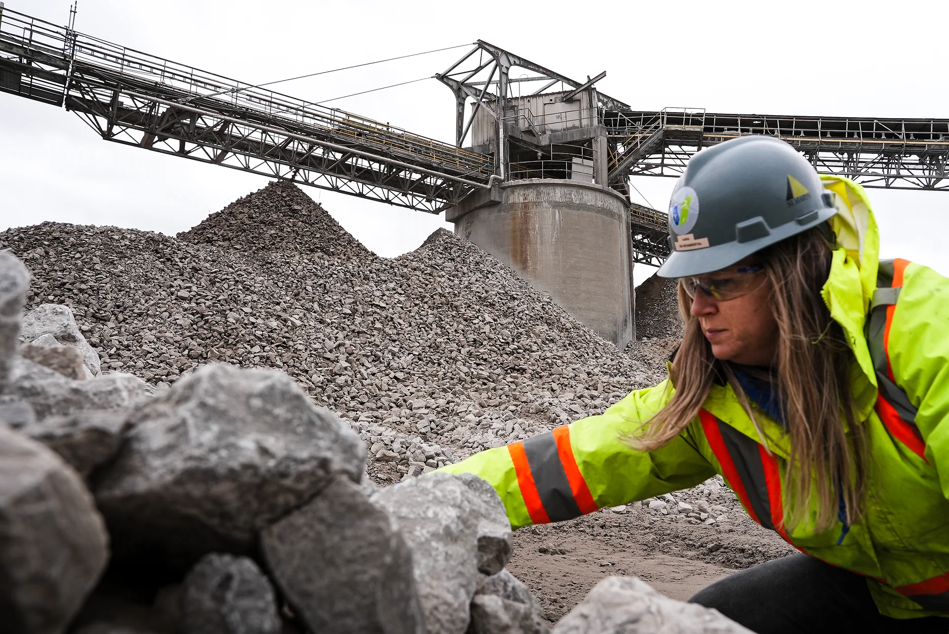 St Marys Cement Plant - team member in a hard hat and hi-vis jacket inspecting crushed stone below a conveyor