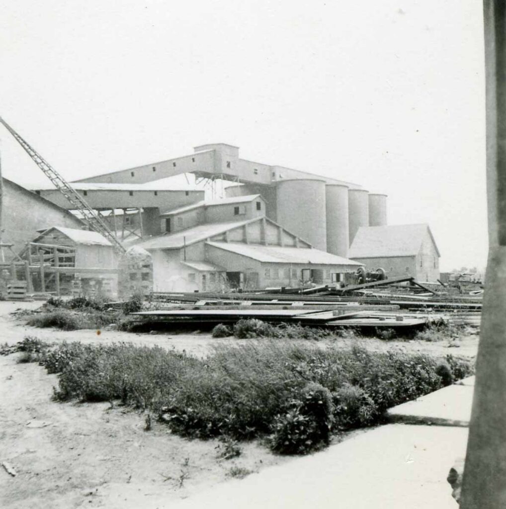Cement Supplier - historic black and white photo of an early cement plant with silos, sheds and a crane