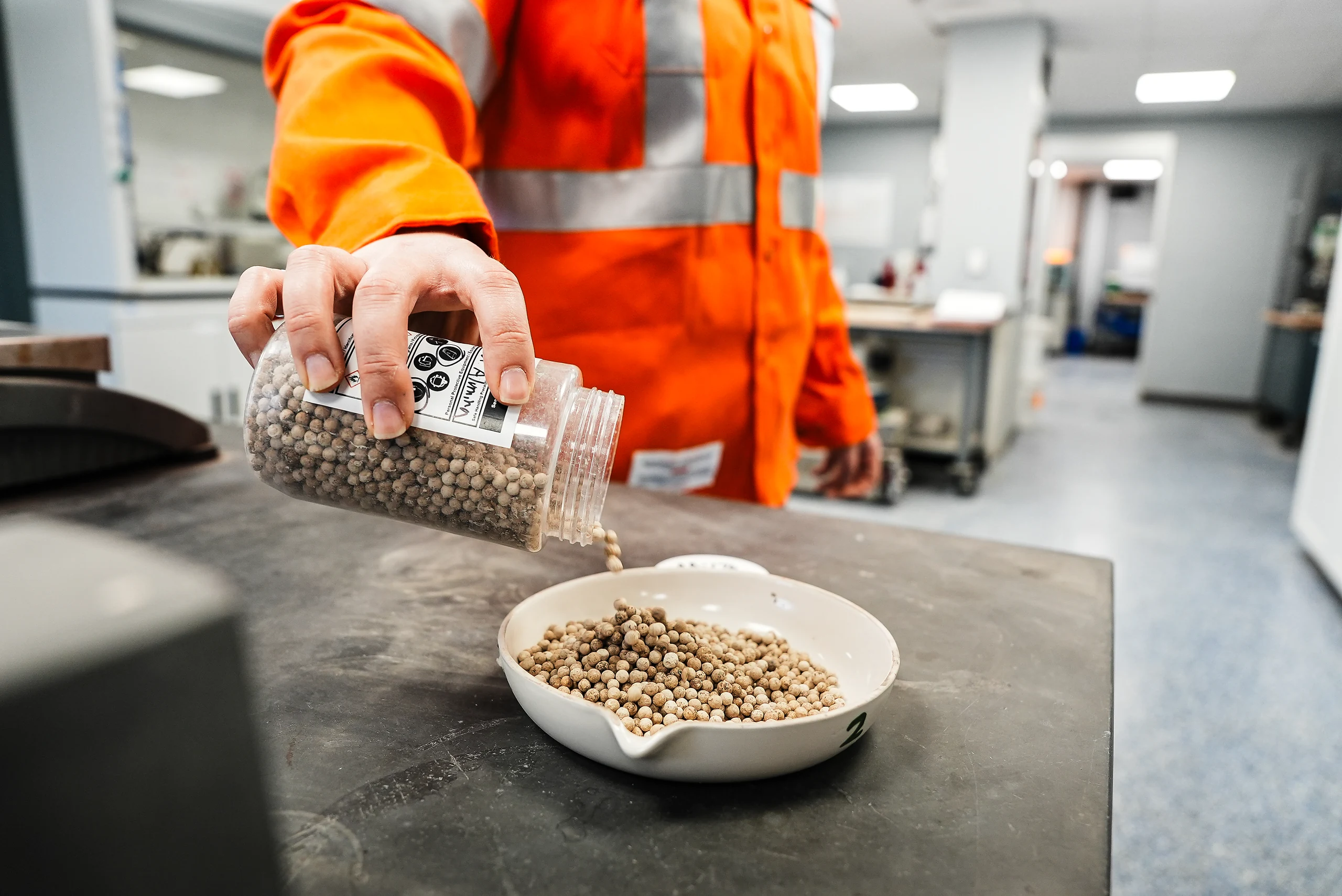 Detroit Cement Plant - lab technician in orange coveralls pouring a pellet sample from a labelled jar into a dish